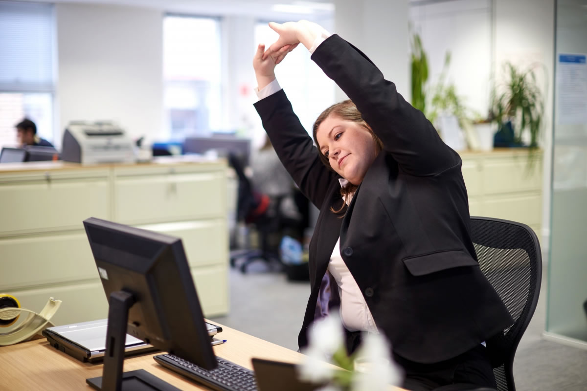 A female office worker stretches whilst sitting at her desk