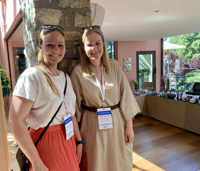 Two female attendees smile for a photograph, there is a buffet setting in the background