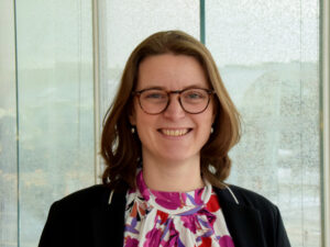 Professional woman smiling in front of a frosted glass background.