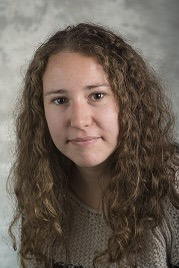 Portrait of a young woman with curly hair against a mottled gray background.