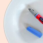 An insulin pen with a blue cap removed is placed on a white plate against a light peach background.