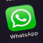 Close-up of the WhatsApp icon on a smartphone screen, showing the green square with a white speech bubble and phone symbol inside, next to other app icons.