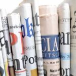 A close-up of various rolled-up newspapers in different languages and fonts, arranged vertically.